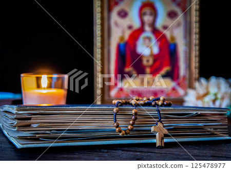 The time for prayer. Wooden Rosary on an ancient prayer book. Icon of the Mother of God and Jesus. Lighted candle The time for prayer. Wooden Rosary on an ancient prayer book. Icon of the Mother of God and Jesus. Lighted candle 125478977