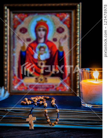The time for prayer. Wooden Rosary on an ancient prayer book. Icon of the Mother of God and Jesus. Lighted candle 125478978