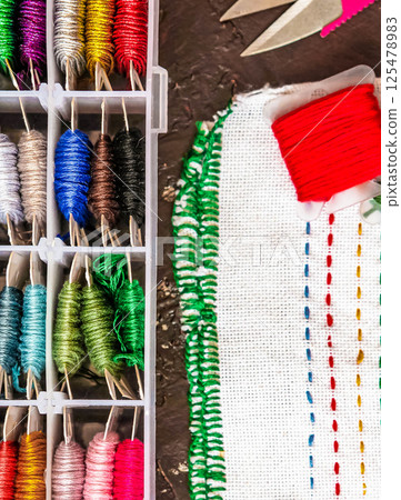 Set of multi-colored cotton threads and fragment of colorful cross-stitch embroidere. Colorful mouline threads. Top view 125478983