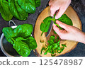 A woman is cutting fresh spinach on a cutting board 125478987