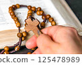 Hand holding and praying on rosary, on Bible background 125478989