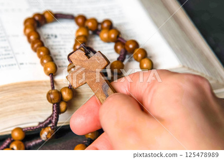 Hand holding and praying on rosary, on Bible background 125478989