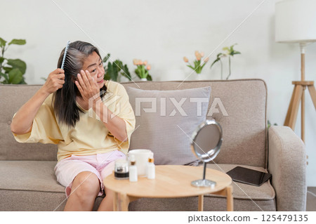 Beauty and Age Diversity. A senior woman applying skincare while combing her hair. 125479135