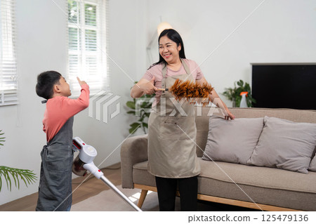 Family Cleaning and Joyful Engagement. A mother and son share a moment while cleaning their living space. Family Cleaning and Joyful Engagement. A mother and son share a moment while cleaning their living space. 125479136