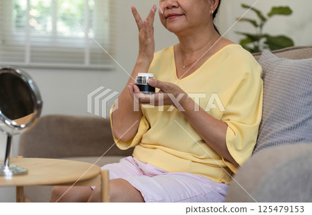 Beauty and Age Diversity. A senior woman applying cream, emphasizing her skincare routine and self-love. Beauty and Age Diversity. A senior woman applying cream, emphasizing her skincare routine and self-love. 125479153