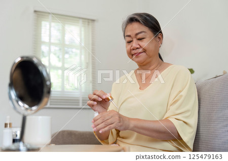 Beauty and Self-Care. An elderly woman applying serum, enjoying her skincare routine at home. 125479163