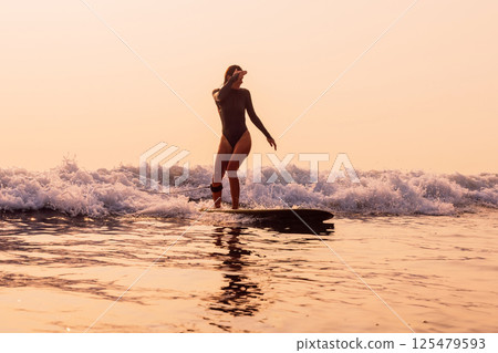 Woman on surfboard on foam wave with warm sunrise or sunset sunlight. 125479593