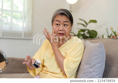 Beauty and Age Diversity. A senior woman applying eye cream, focusing on her skincare routine. Beauty and Age Diversity. A senior woman applying eye cream, focusing on her skincare routine. 125479859