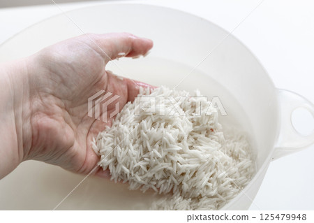 Woman's hand washing white rice in a bowl of water 125479948