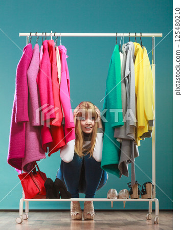 Scared woman hiding among clothes in mall wardrobe 125480210