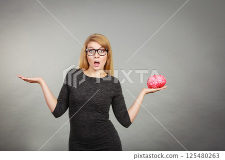 Woman in eyeglasses being confused holding brain Woman in eyeglasses being confused holding brain 125480263