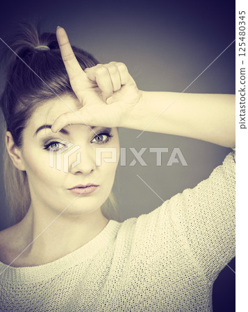 Woman showing loser gesture with L on forehead 125480345