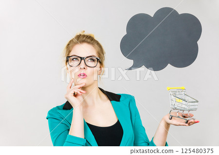 Thinking business woman holding small tiny shopping cart 125480375