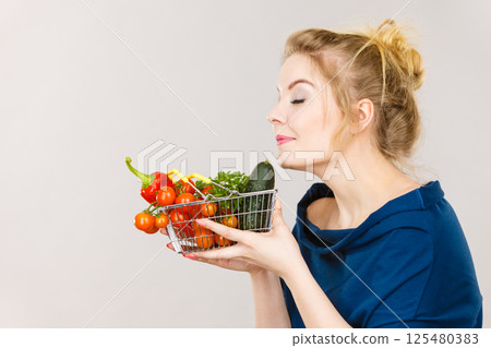 Woman holds shopping basket with vegetables, smelling Woman holds shopping basket with vegetables, smelling 125480383