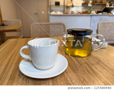 Glass teapot with herbal infusion and white ceramic cup on cafe table. Relaxation and modern tea culture Glass teapot with herbal infusion and white ceramic cup on cafe table. Relaxation and modern tea culture 125480440