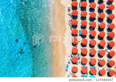 Aerial view of colorful umbrellas on beach, people in blue sea 125480897