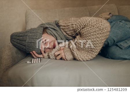 Young woman wearing scarf has flu ill sick disease cold at home indoor on sofa Young woman wearing scarf has flu ill sick disease cold at home indoor on sofa 125481209