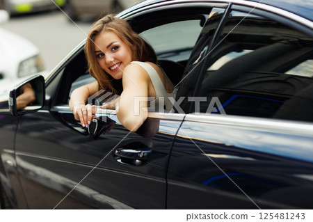 Happy woman driver with key car smiling. Cute young happy brunette female driving car vehicle 125481243