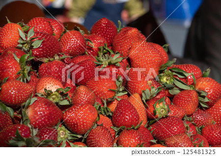 A vibrant collection of ripe, juicy strawberries fills the market stall, reflecting the sunshine. Fresh organic strawberries on market stall. Stall of fresh strawberries. 125481325