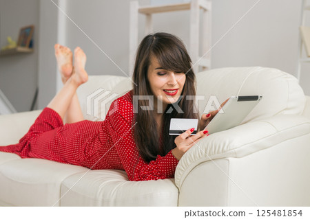 Woman uses credit card and tablet to shop online from home sofa. Digital commerce, consumer ease and modern shopping 125481854