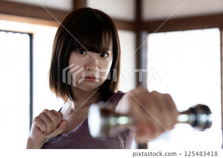 A young woman training with a dumbbell 125483418