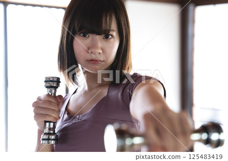 A young woman training with a dumbbell 125483419