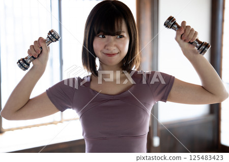 A young woman training with a dumbbell 125483423
