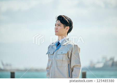 A young man in his 20s wearing work clothes gazing into the distance 125485380