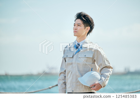 A young man in his 20s wearing work clothes gazing into the distance 125485383