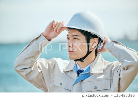 A young man in his 20s wearing work clothes and a helmet 125485386