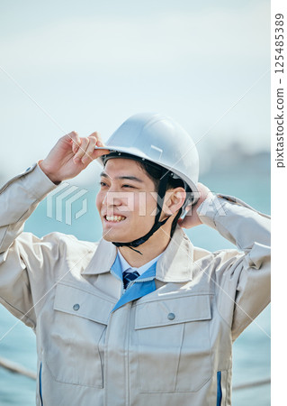 一名 20 多歲的年輕男子穿著工作服,戴著頭盔 一名 20 多歲的年輕男子穿著工作服,戴著頭盔 125485389