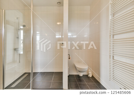 A sleek and contemporary bathroom featuring a glass shower, toilet, and minimalist design with white tiles and dark flooring. 125485606