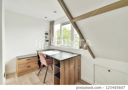 A stylishly designed home office featuring a wooden desk and elegant chair, illuminated by natural light from large windows. 125485607