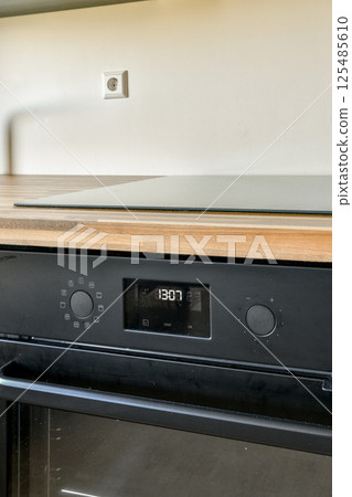 A sleek cooktop featuring a digital display and control knobs, set against a wooden countertop, showcasing contemporary kitchen design aesthetics. A sleek cooktop featuring a digital display and control knobs, set against a wooden countertop, showcasing contemporary kitchen design aesthetics. 125485610