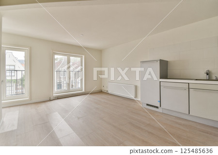 A bright and modern minimalist kitchen and living area featuring large windows, neutral colors, and streamlined design elements for a spacious feel. 125485636