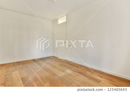 A spacious, empty room featuring light-colored walls and wooden flooring, showcasing a minimalist interior design that emphasizes simplicity and openness. 125485643