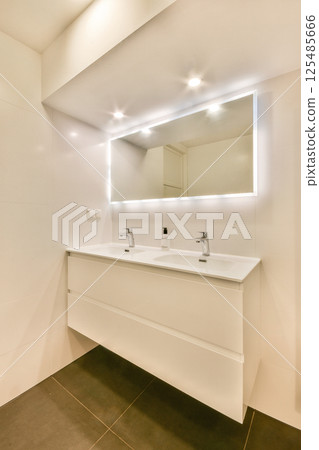 A sleek and contemporary bathroom featuring a clean white vanity, dual sinks, and illuminated mirror. The space emphasizes a minimalistic aesthetic. 125485666