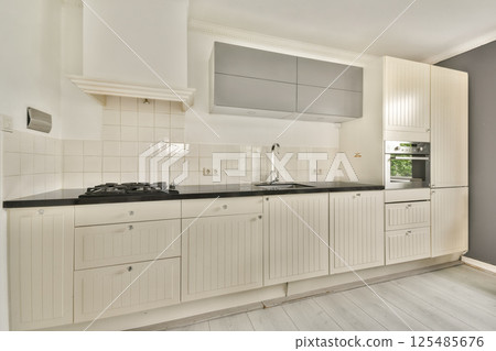 Spacious and sleek kitchen featuring white cabinetry, black countertops, and modern appliances, creating an inviting culinary space. 125485676