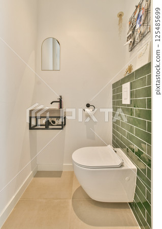 A sleek bathroom featuring a modern toilet and a stylish green tile accent wall. The minimalist design provides a clean and refreshing aesthetic. 125485699