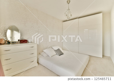 A serene and stylish bedroom featuring a minimalist design, with a white color palette, elegant furnishings, and ample natural light for a calming ambiance. 125485711