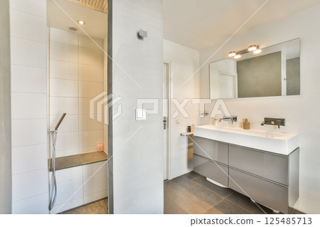 Contemporary bathroom featuring a sleek shower area and stylish vanity, complemented by elegant lighting and minimalistic decor for a serene atmosphere. 125485713