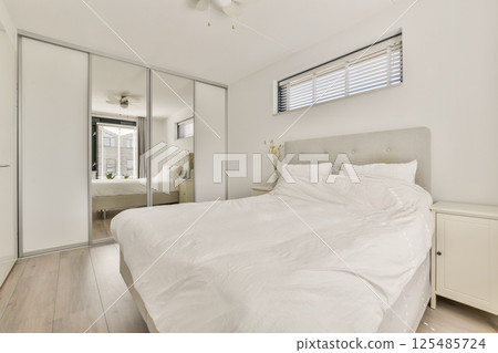 A bright and airy modern bedroom featuring a large bed, stylish decor, and ample natural light from windows creating a serene atmosphere. 125485724