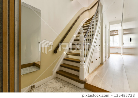 A beautifully designed staircase with a white balustrade and soft lighting, enhancing the elegance of the interior space. Ideal for modern home decor inspiration. A beautifully designed staircase with a white balustrade and soft lighting, enhancing the elegance of the interior space. Ideal for modern home decor inspiration. 125485728