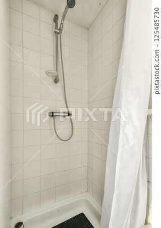 A clean and contemporary shower featuring white tiled walls and a sleek shower head, complemented by a curtain for privacy. 125485730