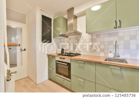 A contemporary kitchen featuring sleek green cabinets, a modern stove, and a minimalist design. Natural light enhances the clean aesthetic, making it inviting. 125485736
