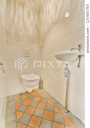 A clean and minimalist bathroom featuring white tiled walls, a stylish toilet, and a sleek sink, showcasing a harmonious combination of design and functionality. 125485763