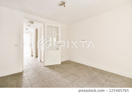 an empty room with tile flooring and white walls in a door is on the right side of the room 125485765