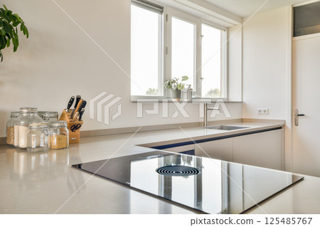 A sleek and modern kitchen design featuring a clean, minimalist aesthetic, large windows letting in natural light, and stylish appliances. A sleek and modern kitchen design featuring a clean, minimalist aesthetic, large windows letting in natural light, and stylish appliances. 125485767