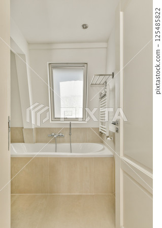A stylish modern bathroom featuring a bathtub, sleek fixtures, and a large window for natural light. The interior design emphasizes cleanliness and simplicity. A stylish modern bathroom featuring a bathtub, sleek fixtures, and a large window for natural light. The interior design emphasizes cleanliness and simplicity. 125485822