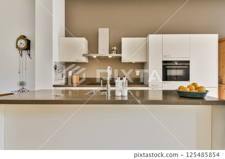 Sleek, modern kitchen featuring a minimalist aesthetic with white cabinetry, a simple countertop, and fresh fruit display, creating a clean and inviting space. Sleek, modern kitchen featuring a minimalist aesthetic with white cabinetry, a simple countertop, and fresh fruit display, creating a clean and inviting space. 125485854